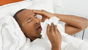 A sick man sneezing into tissues while lying in bed