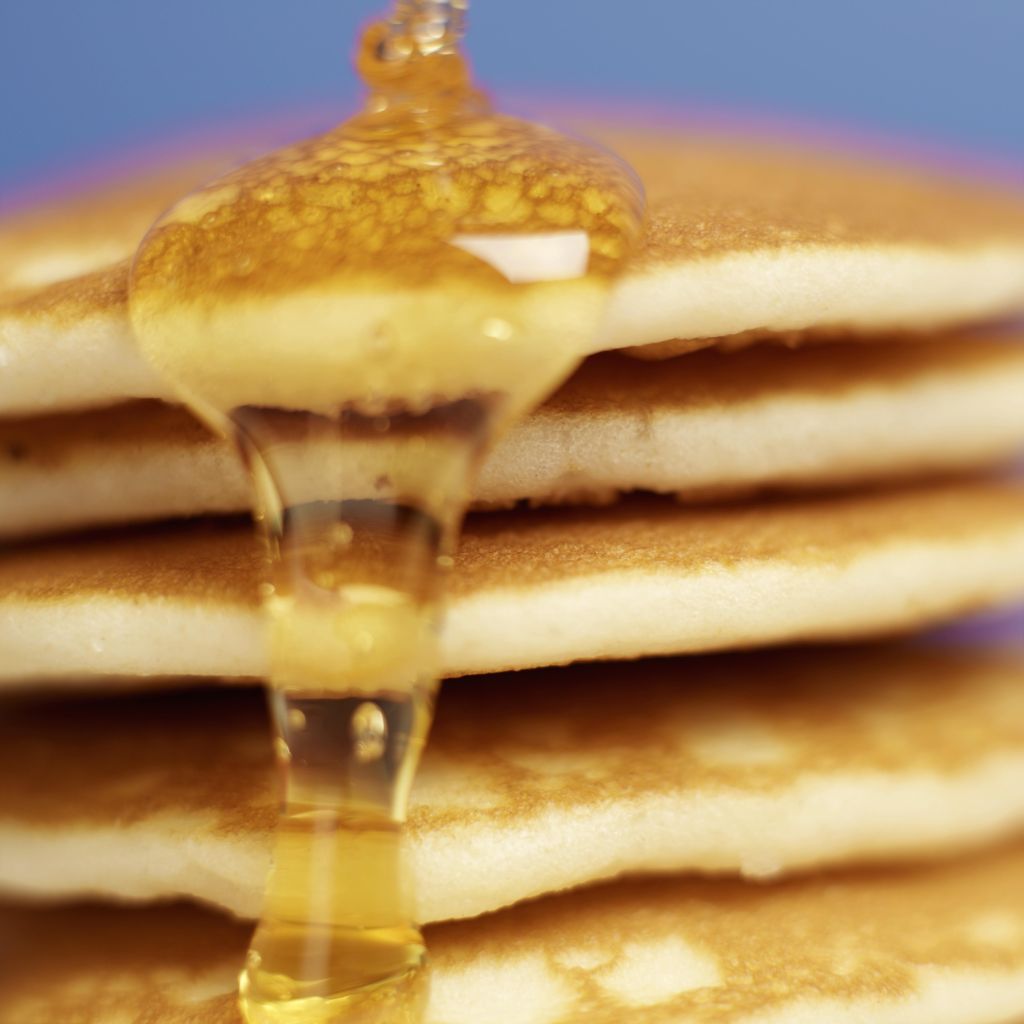Close-up of pancakes stacked high with syrup being poured over them