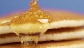 Close-up of pancakes stacked high with syrup being poured over them