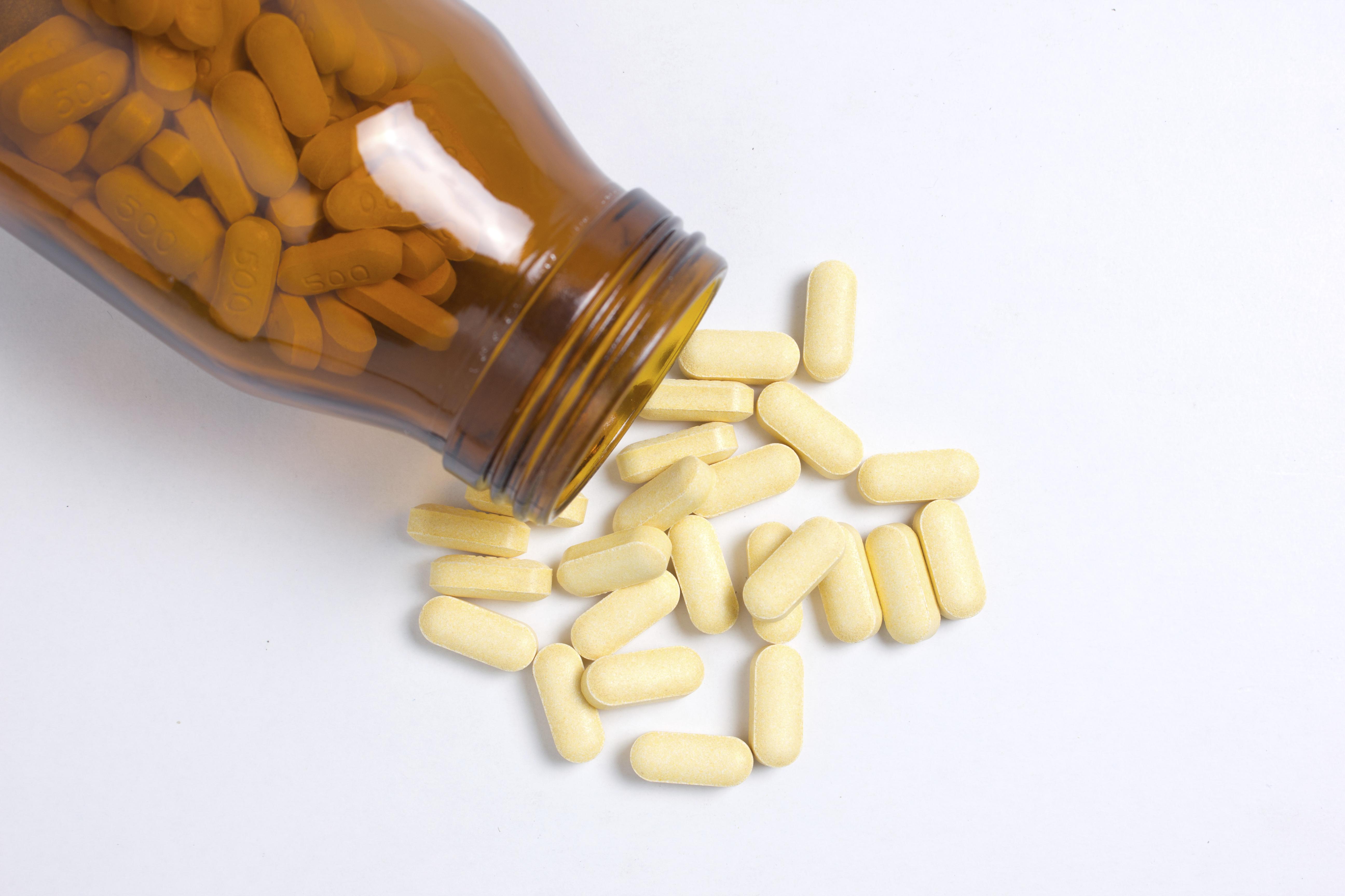 Prescription pill bottle spilling pills on to surface isolated on a white background.