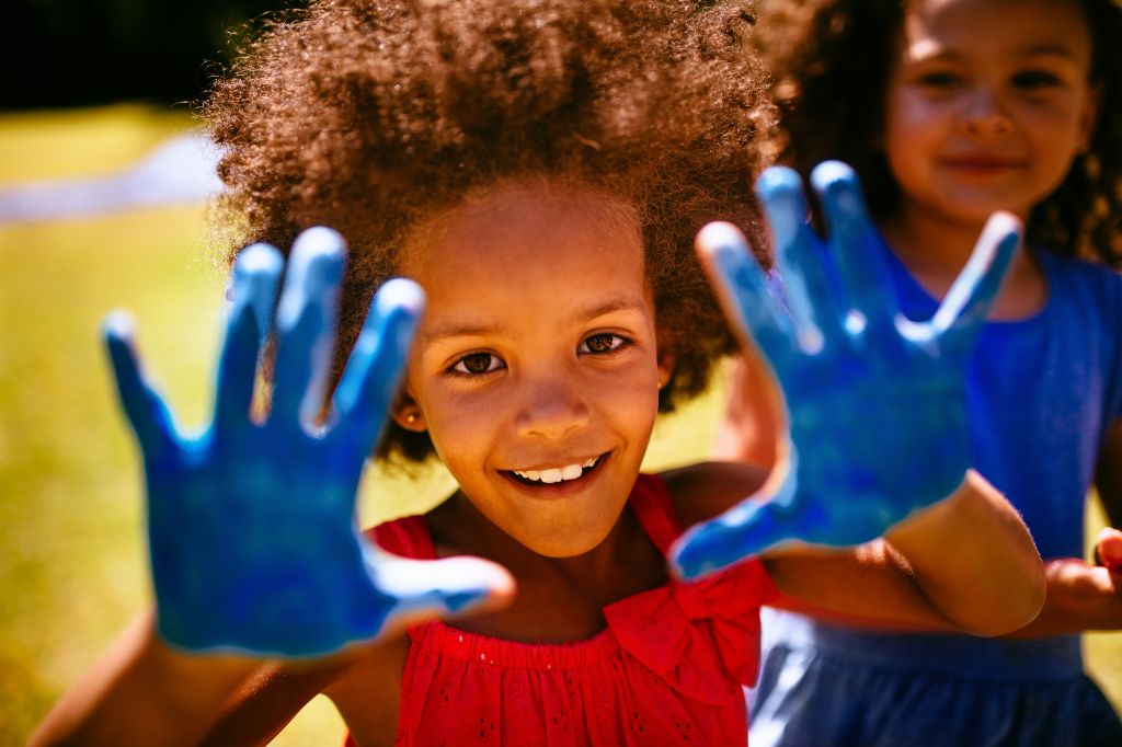 Little Afro girl showing hands full of blue paint