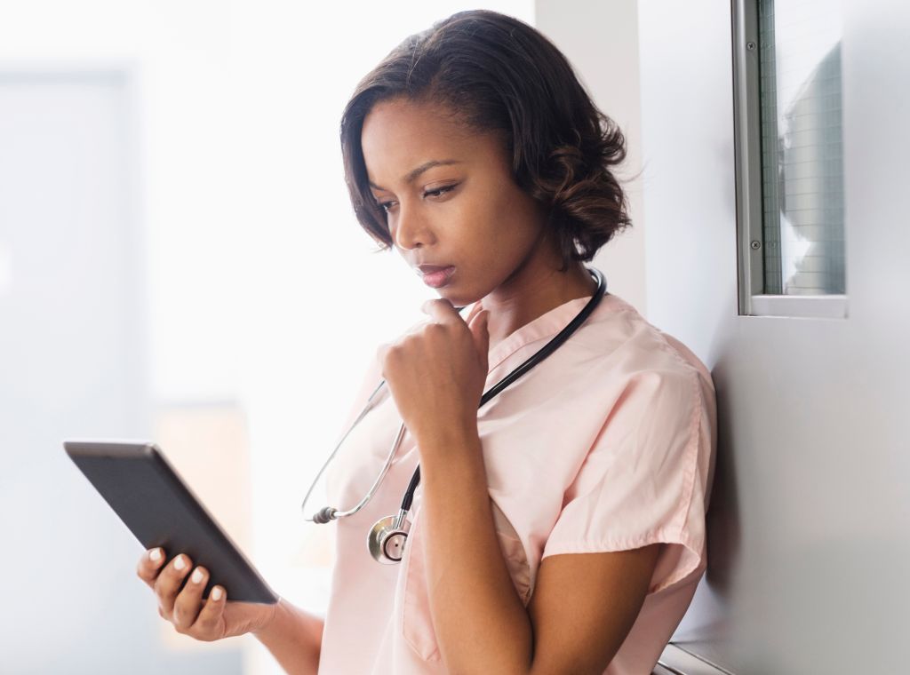 Mixed Race nurse using digital tablet leaning on door