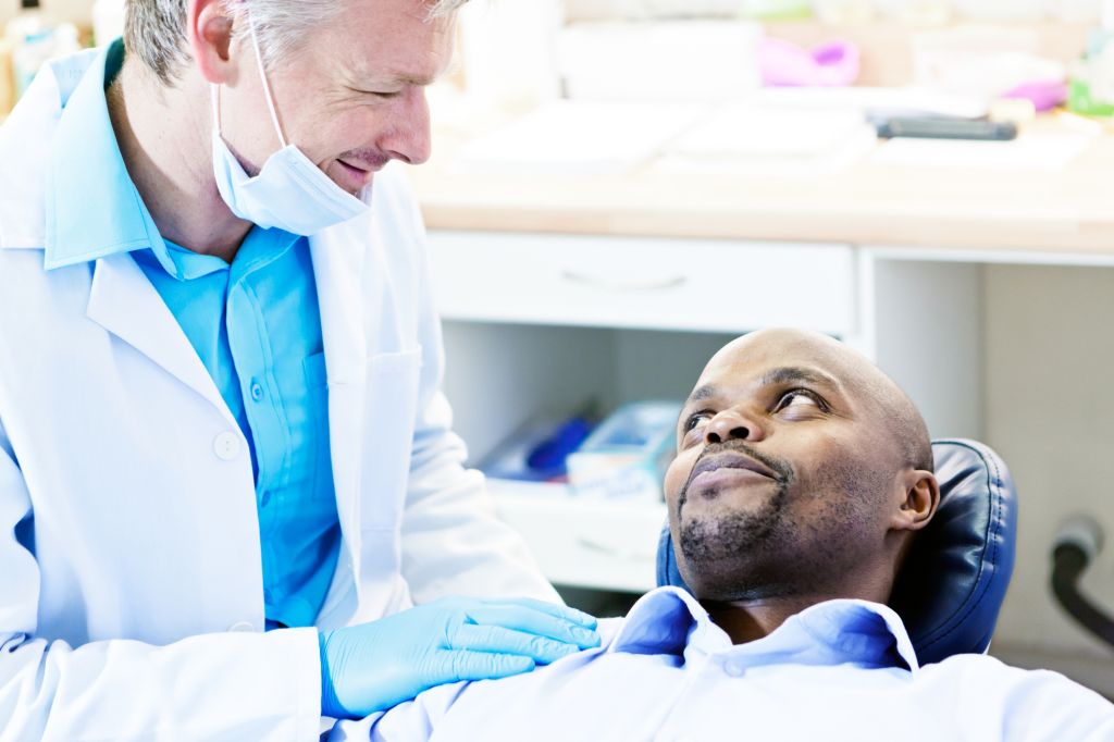 Smiling dentist reassures male dental patient in the chair