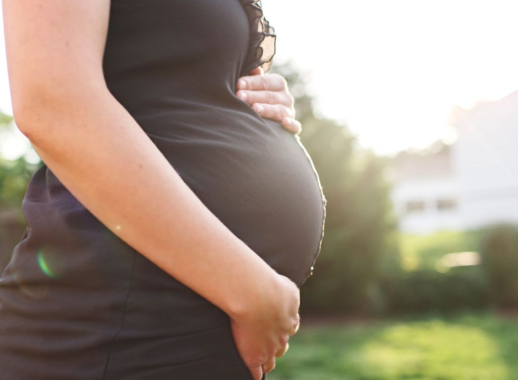 Side view of pregnant woman standing outdoors, one hand on top of her pregnant belly and one hand underneath the bump.