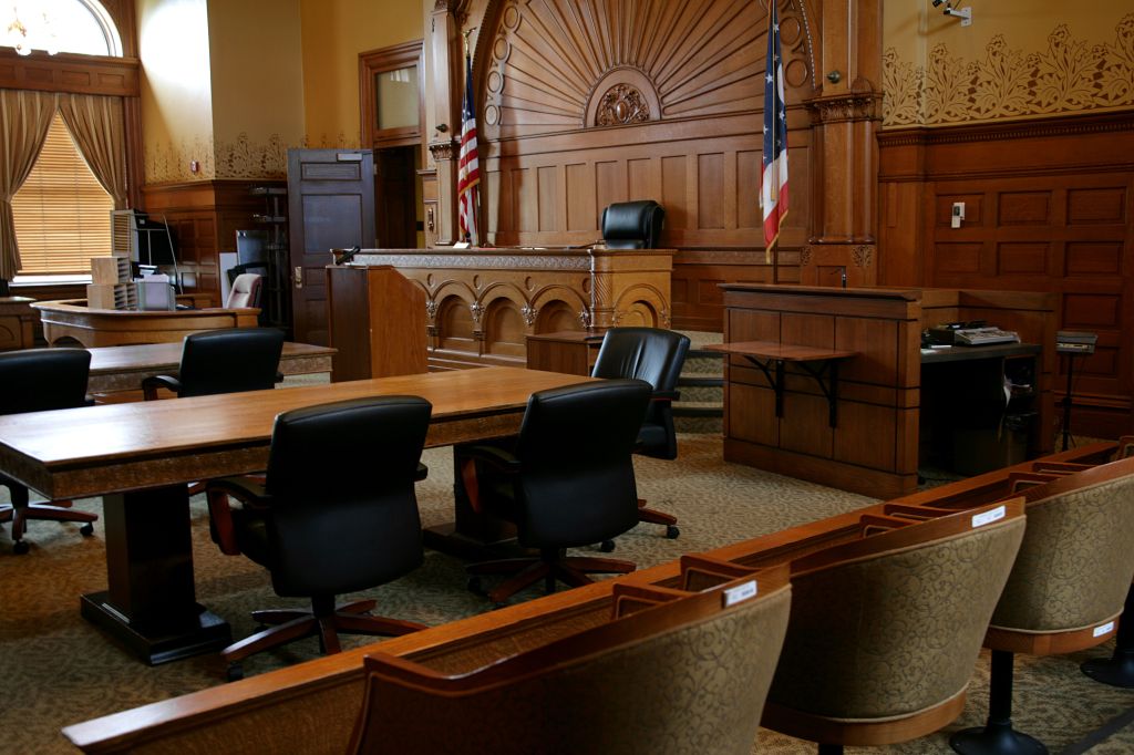 An empty, brown-paneled courtroom with flags