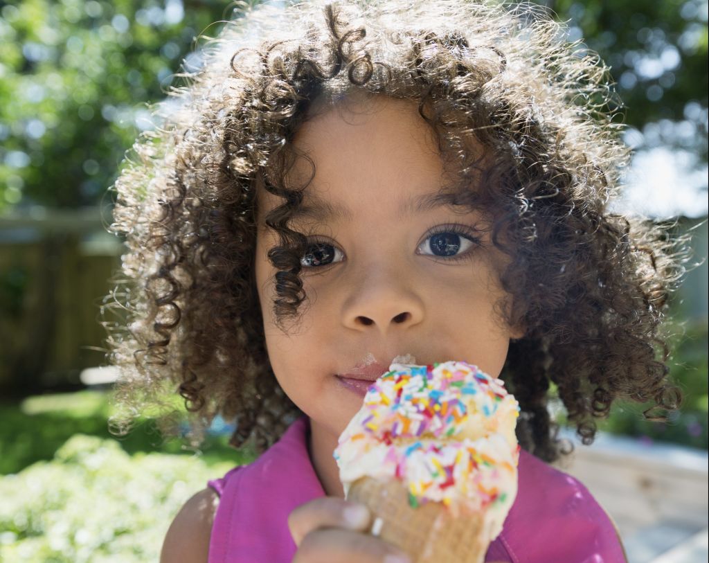 Close up portrait girl eating ice cream cone with sprinkles in sunny backyard