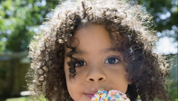 Close up portrait girl eating ice cream cone with sprinkles in sunny backyard