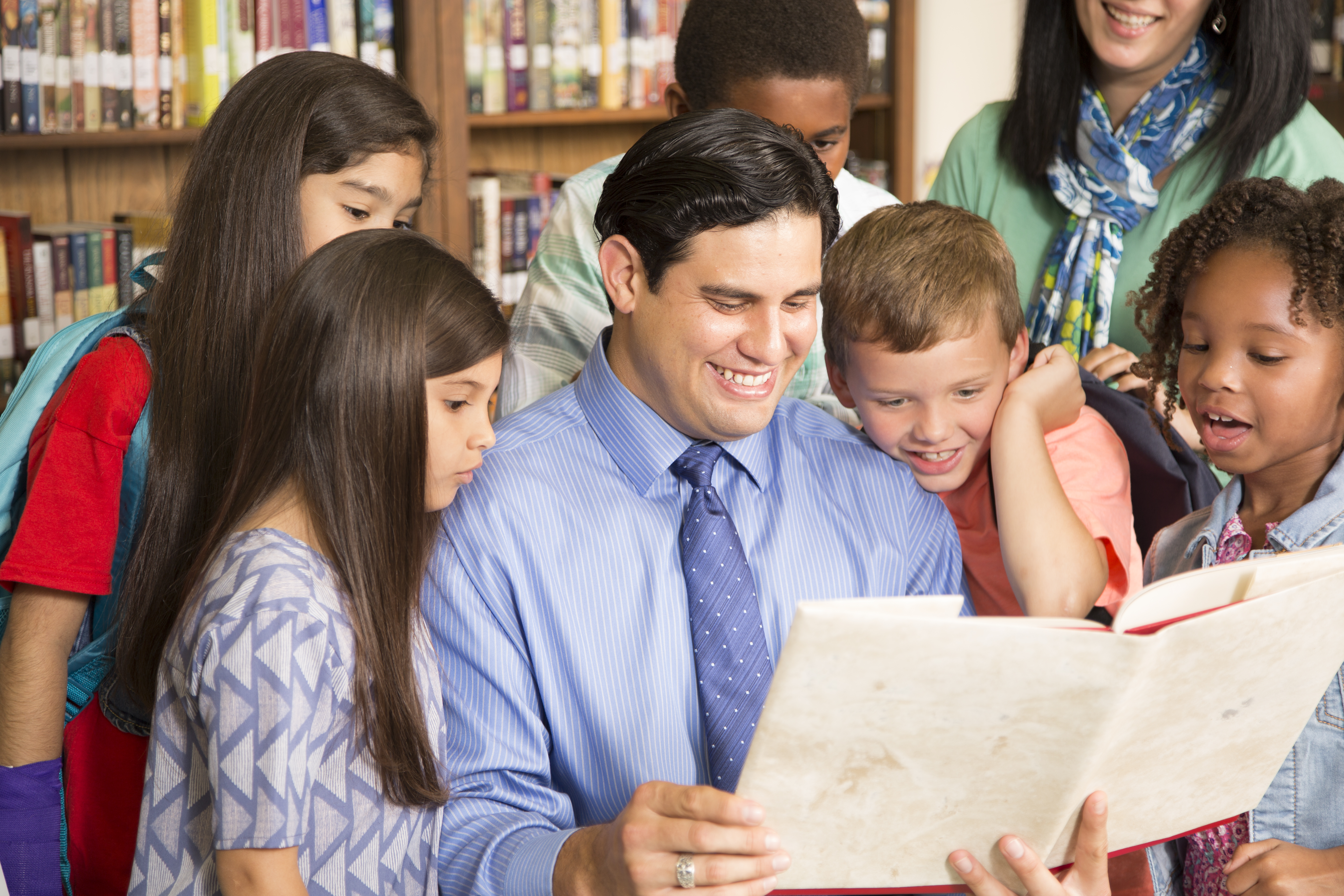 Teacher, librarian reads book to elementary students in library or classroom.