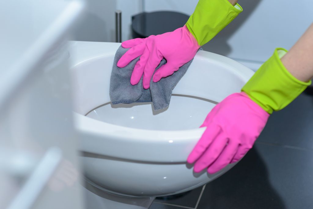 Cropped Hands Of Woman Cleaning Toilet Bowl In Bathroom