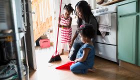 Daughters helping mother sweep kitchen floor
