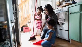 Daughters helping mother sweep kitchen floor