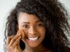 Beautiful black woman applying compact powder on her face looking at camera smiling