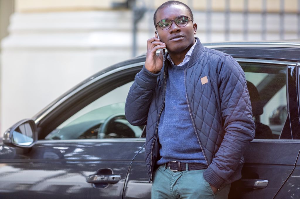 Portrait of young man on the phone leaning against car