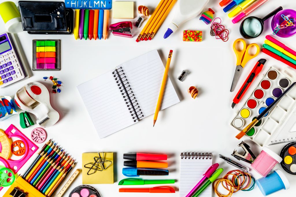 Overhead shot of back to school office supplies on white background with paper note book into frame.