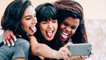 Three girl friends making funny faces for a selfie with cell phone