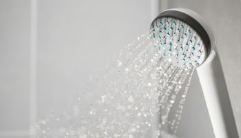 Close-Up Of Shower Head Spraying Water In Bathroom