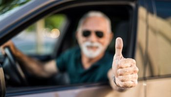 Senior man in car showing thumb up focus on foreground.