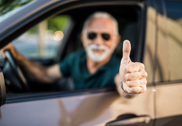 Senior man in car showing thumb up focus on foreground.