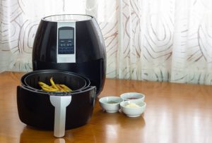 Air fryer with French fries on a table with sauces and spices