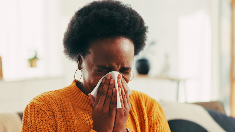 Blowing nose, sick and black woman in home with flu, cold or allergies with viral infection. Illness, tissue and African female person with sneeze for sinusitis, hayfever or virus in living room.