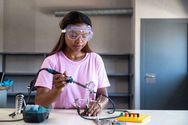Young woman soldering electronics in stem workshop