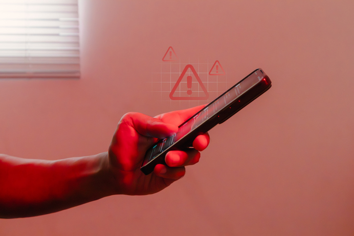 Hand holding a smartphone with warning symbol notification in red light room