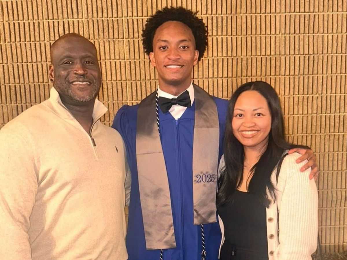 Three people posing for a photo - a smiling man in a beige sweater, a young man in a blue graduation gown, and a smiling woman in a white sweater.